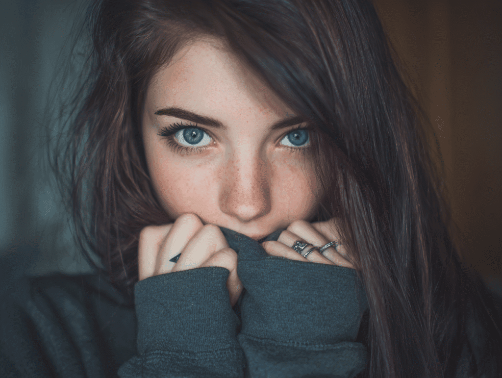 Innocent young woman with striking blue eyes and dark hair in cozy sweater, symbolizing women’s fantasies, desire, and age gap romance dynamics